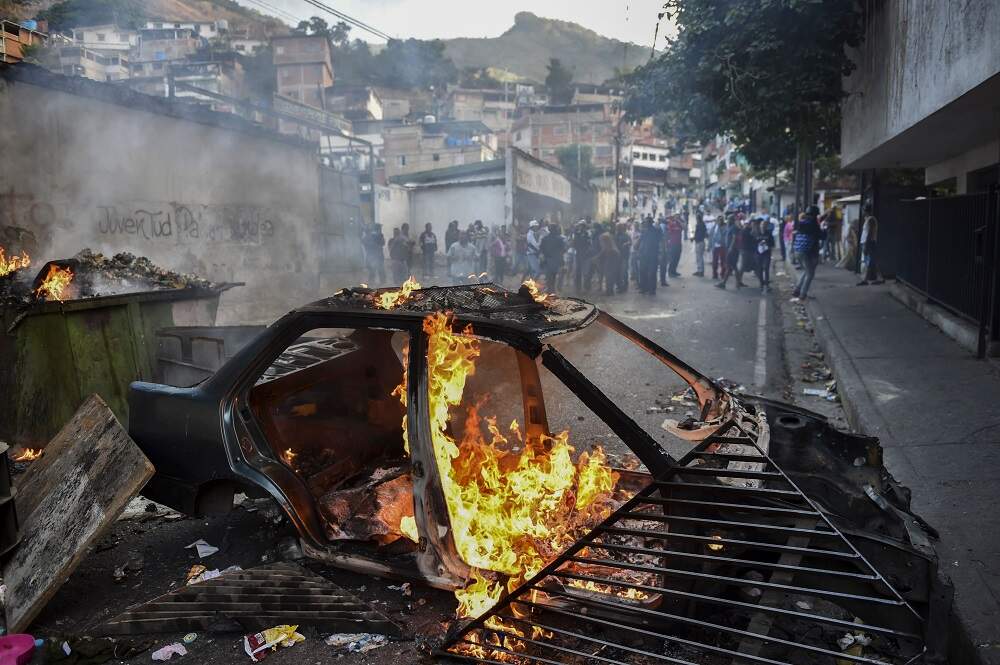 Manifestantes contrários ao governo venezuelano queimam um carro em frente à sede da Guarda Nacional